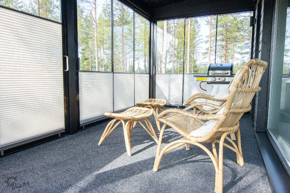 Inglasad altan med solstolar och plisségardiner mot skogen