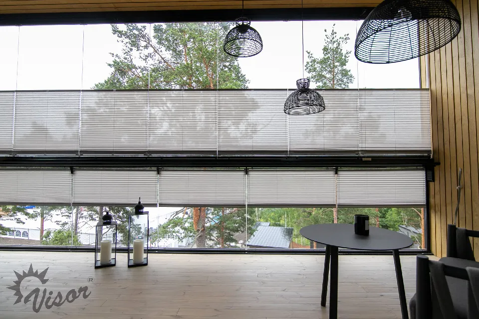 Inglasad altan med matbord och plisségardiner mot skogsutsikt