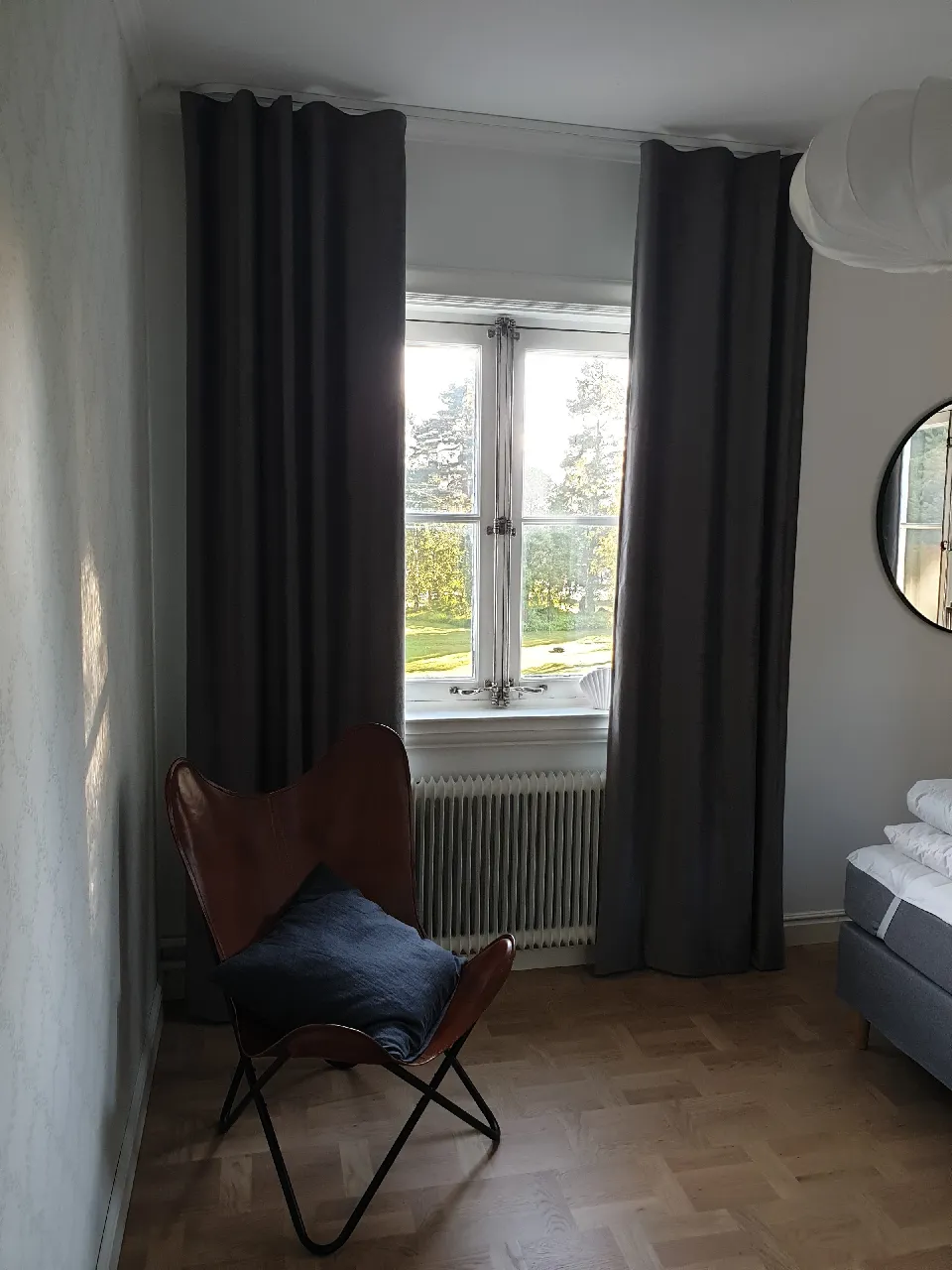 Fåtölj vid ett fönster med gardiner och hissgardin