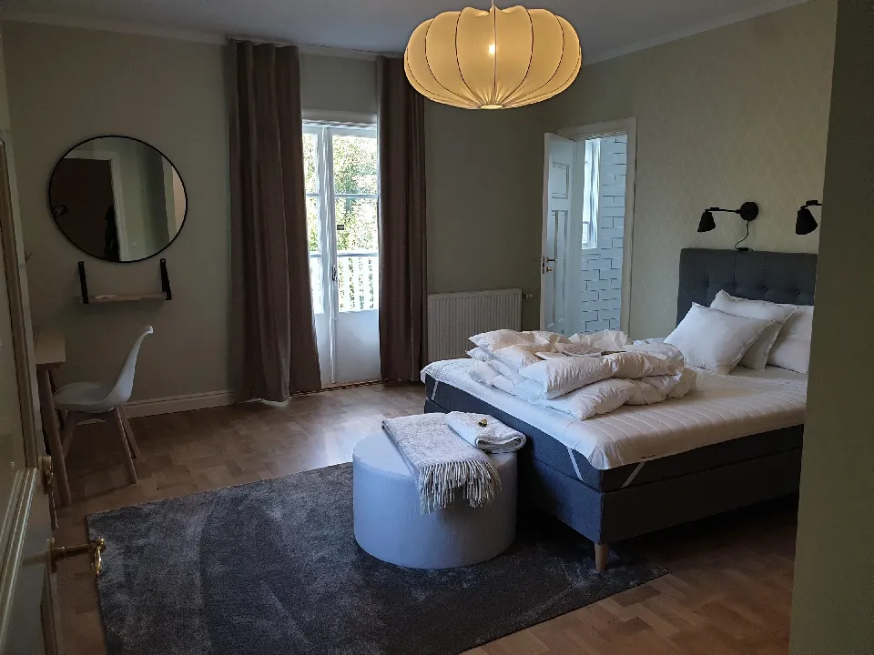 Sovrum med dubbelsäng, rund spegel och gardiner i beige