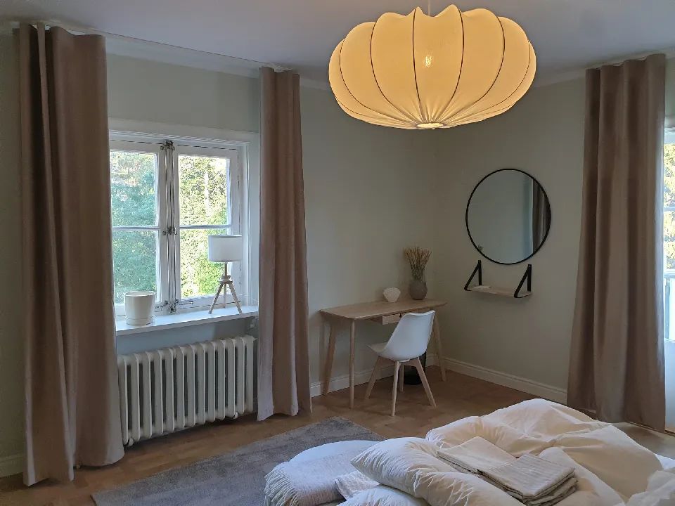 Sovrum med taklampa, skrivbord och gardiner i beige