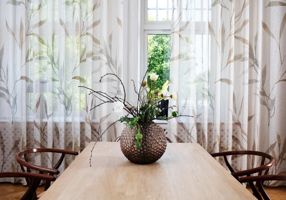 Matbord med blomsterarrangemang framför mönstrade gardiner