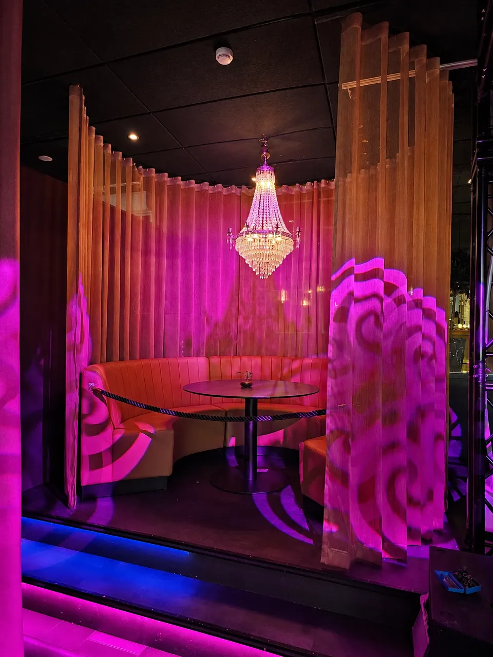 Sittbås i rosa belysning framför gardiner och neonskylt