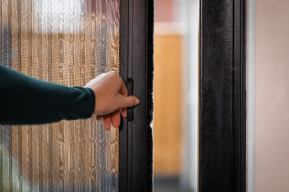 Hand som öppnar ett plisserat insektsnät i en dörr