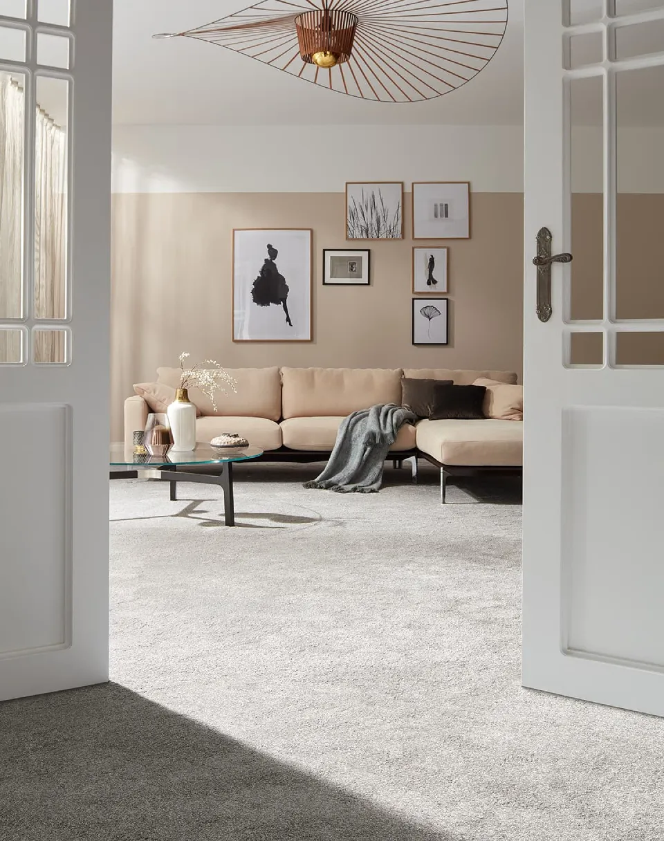 Vardagsrum med beige soffa på en ljusgrå heltäckningsmatta