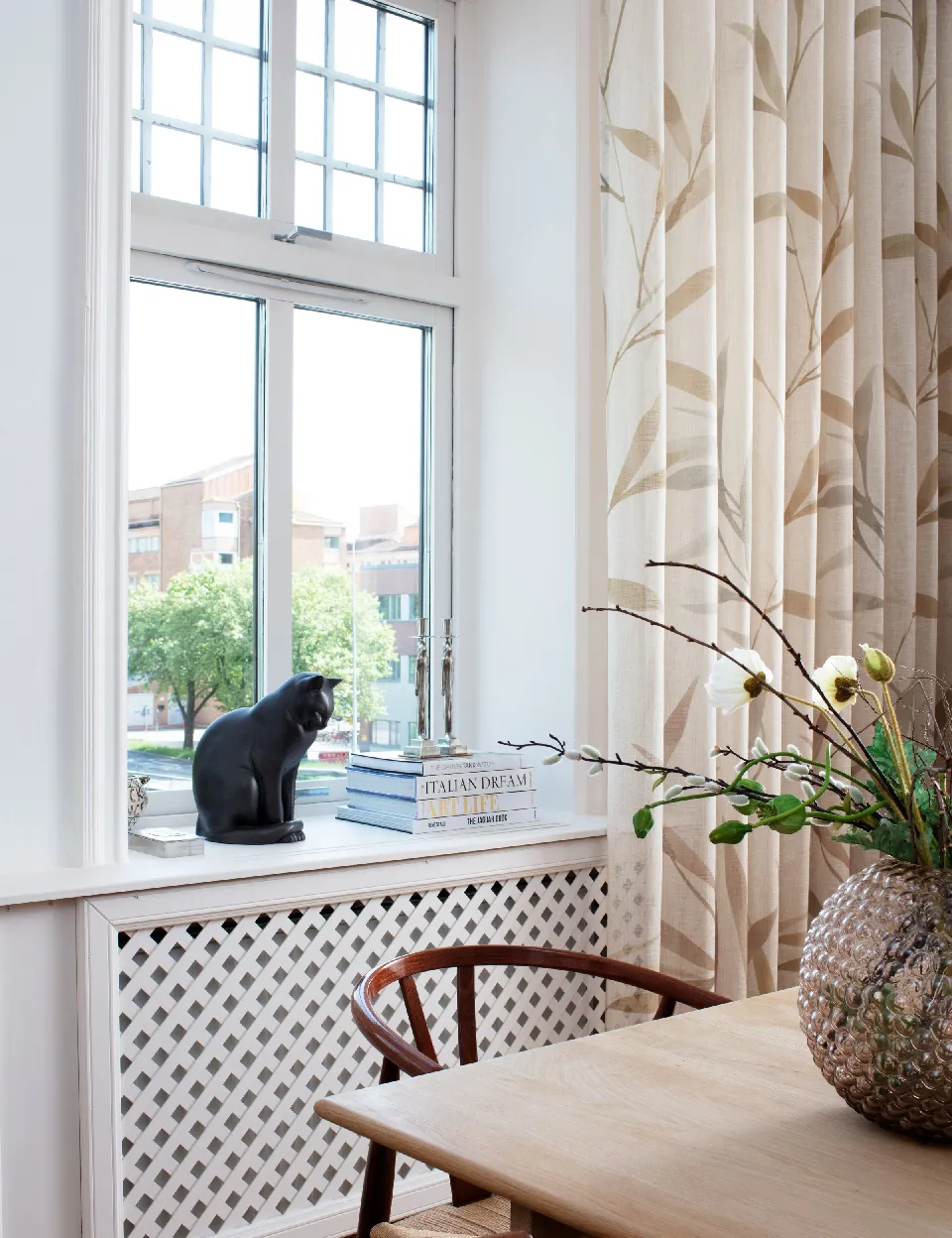 Fönster med kattfigur och gardiner i beige bladmönster