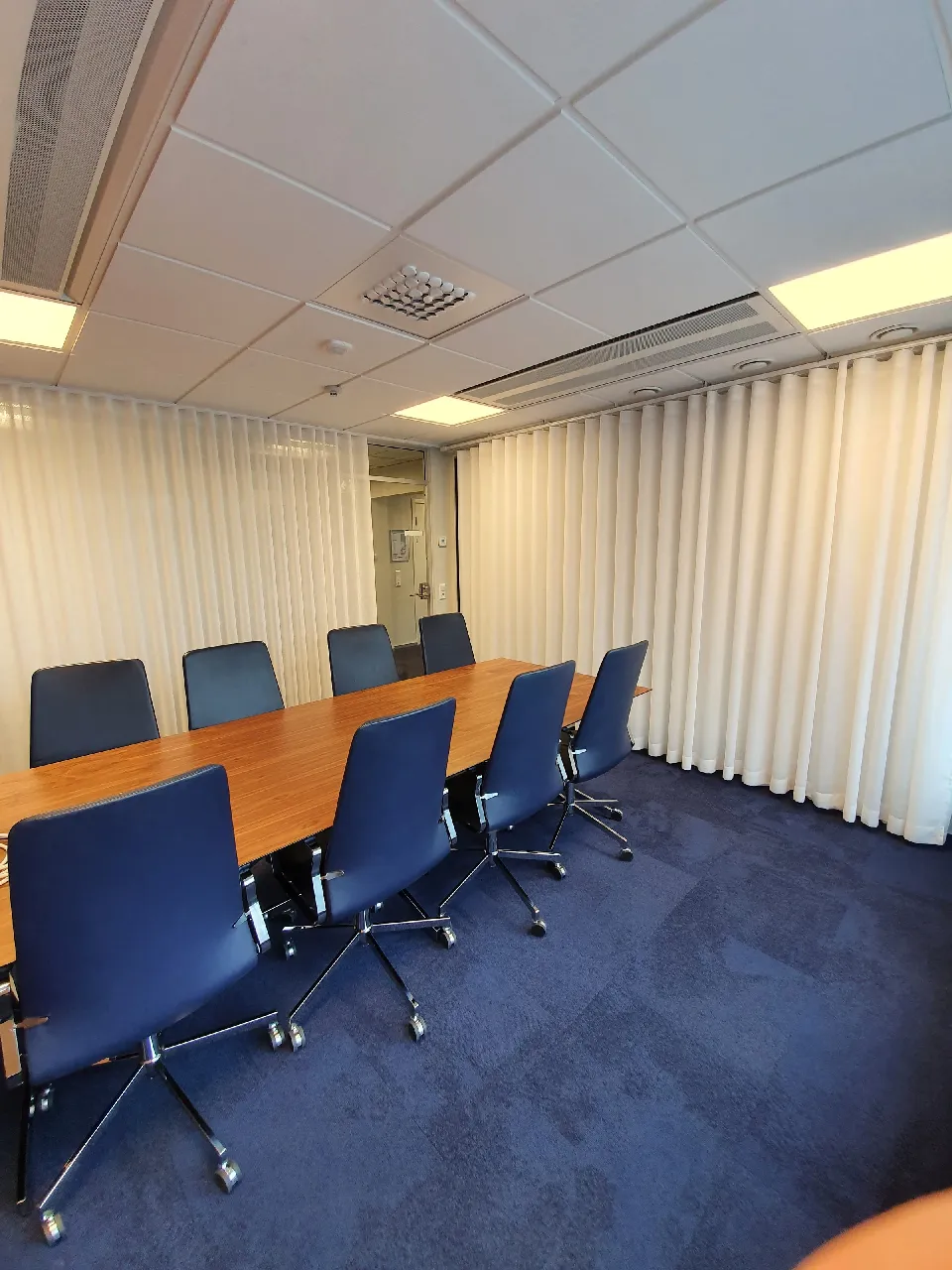 Mötesrum med konferensbord och ljusa gardiner längs fönsterväggen