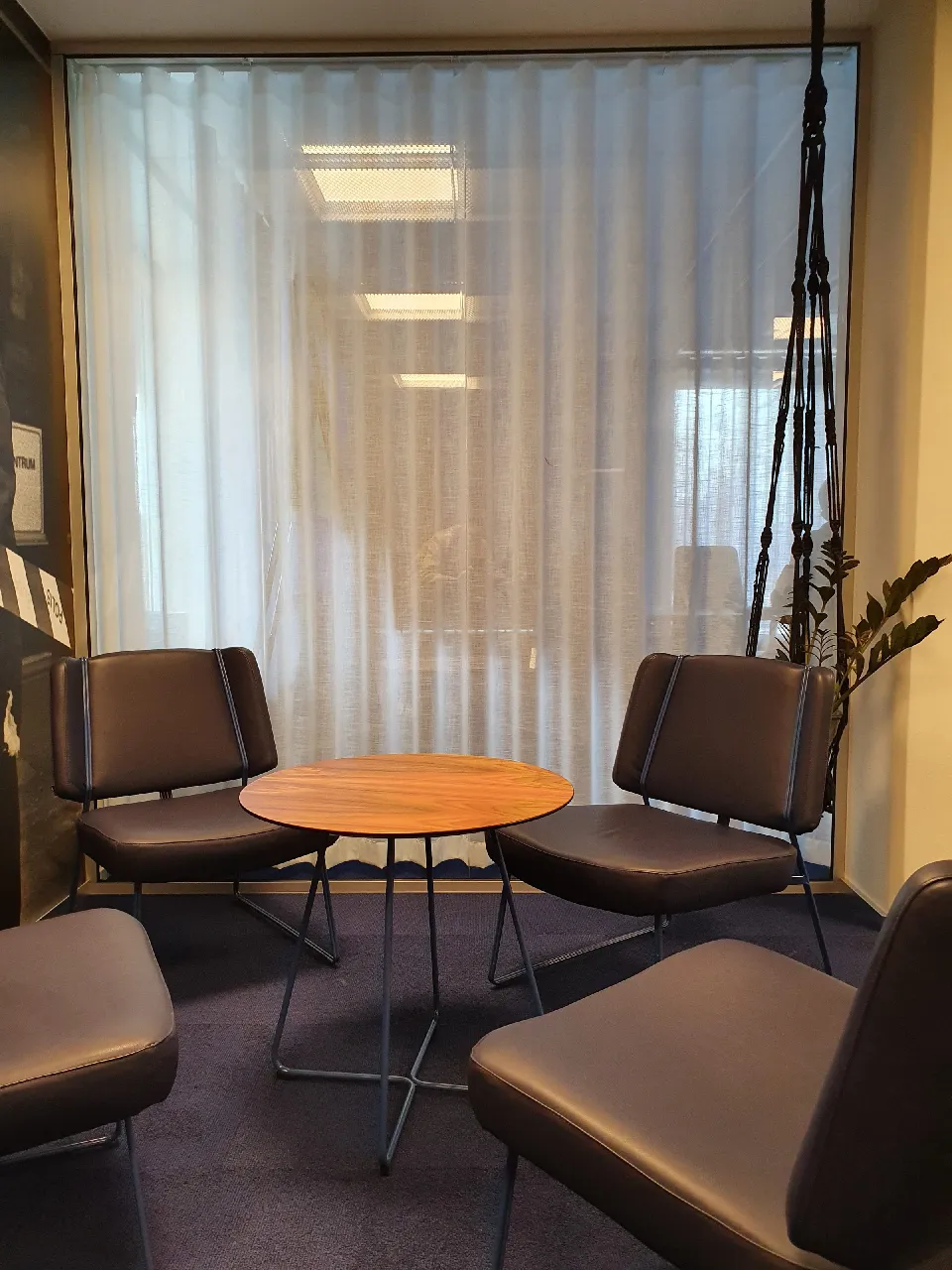 Väntrum med fåtöljer och bord framför ljusa gardiner